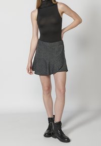 Body de cuello alto negro combinado con una mini falda a cuadros gris que presenta un diseño en capas. Botines negros de cordones completan el conjunto.