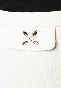 Vit texturerad tyg med ett klaffstängning som har en dekorativ accent av vita pärlor och silverfärgade inslag i en blommig design.