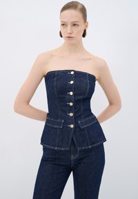 Top in denim senza spalline di colore blu scuro con un design a peplum strutturato. Presenta bottoni dorati e tasche frontali, con dettagli di cucitura a contrasto.