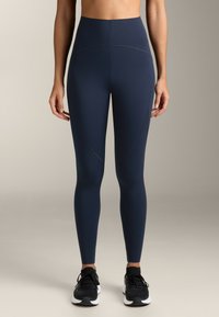 Leggings bleumarin cu talie înaltă, cu o textură neted�ă, având cusături curbate și un design ajustat. Asortați cu pantofi sport negri.