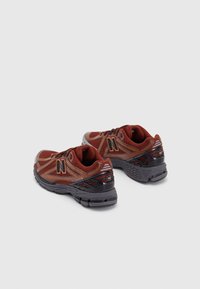 Scarpe sportive rosse e grigie realizzate in rete e materiale sintetico, con una forma leggermente curva e dettagli testurizzati, caratterizzate da un logo prominente.