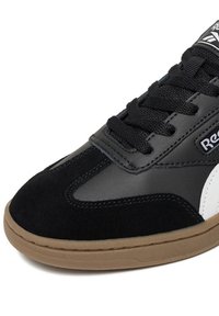 Zapatilla en blanco y negro que combina materiales de cuero y ante, con cordones texturizados y suela de goma de color cáñamo.