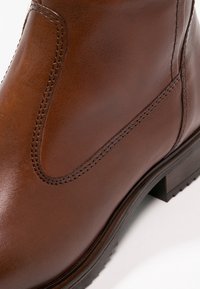 Bottine en cuir marron avec des coutures détaillées et un petit talon empilé sur fond blanc.