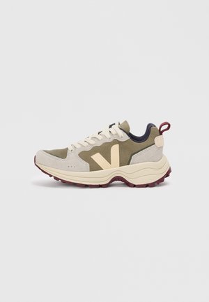 Sneaker verde e beige realizzato con materiali in suede e mesh, dotato di una suola voluminosa, logo prominente sul lato e dettagli in colore marsala.