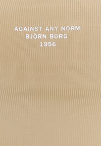 Bežová ribbovaná látka s bílým vyšitým textem "PROTI VŠEM NORMÁM BJÖRN BORG 1956" umístěným uprostřed povrchu.