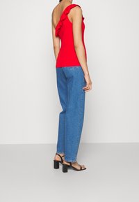 Top rojo off-the-shoulder con detalle de volantes, combinado con jeans rectos de pierna ligera azul y sandalias negras de tacón cuadrado.