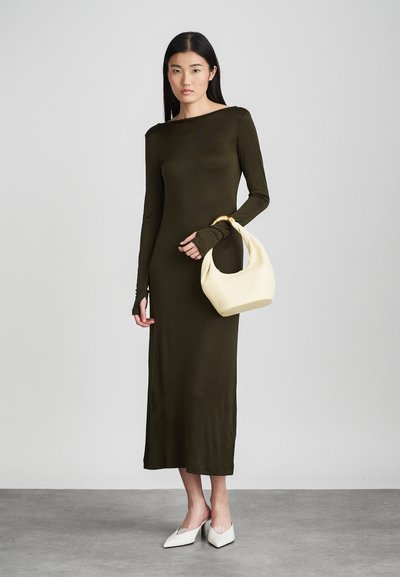 Ελιάς πράσινο φόρεμα μακρύ μανίκι με εφαρμοστή σιλουέτα, στρογγυλή λαιμόκοψη και τρύπες για τους αντίχειρες. Συνδυάζεται με μια κρεμ τσάντα hobo και λευκά μυτερά σαμπό.