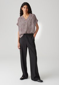 Blouse ample avec un col en V, ornée d'un motif abstrait rouge et blanc, associée à un pantalon noir taille haute et des chaussures noires plates.