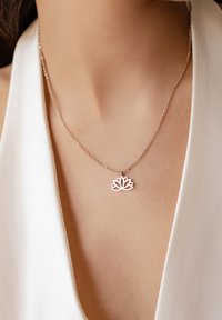 Collana d'argento con pendente a forma di loto, catena delicata, texture liscia e design minimalista, indossata su uno sfondo di tessuto chiaro.