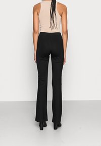 Svarta utsvängda byxor med en åtsittande siluett, gjorda av stretchmaterial. Parat med en beige ärmlös topp. Slät textur, inga synliga mönster.