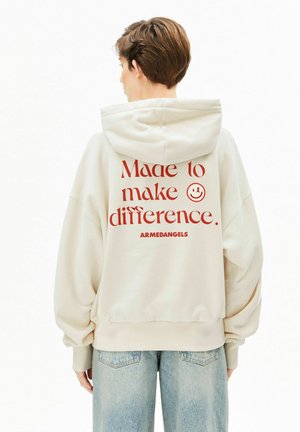 Sweat à capuche crème avec texte rouge « Made to make difference » et visage souriant au dos. Coupe décontractée, matériau doux, capuche ajustable.