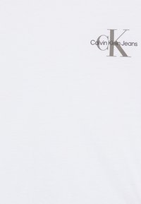 Calvin Klein Jeans white cotton t-shirt featuring a silver logo with "CK" and "Calvin Klein Jeans" printed on the left chest area.