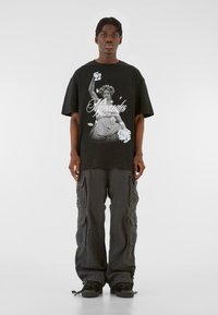 Sort grafisk t-shirt med hvidt print af en klassisk statue og dekorativ tekst. Sammensat med mørke cargo-bukser og sorte sko.