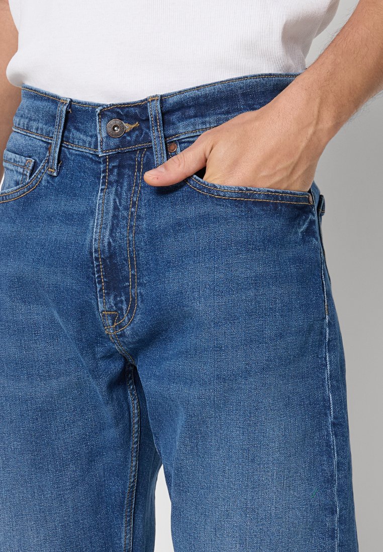 Dunkelblaue Jeans aus Denim mit einem klassischen Schnitt, sichtbaren Nähten und einer Hosentasche. Der Stoff hat eine glatte Textur.