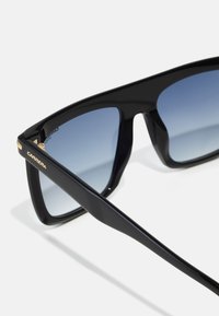 Ochelari de soare supradimensionați, negri, cu lentile gradient de culoare albastră. Ramele au un finisaj lucios, iar templele sunt accentuate cu detalii aurii.