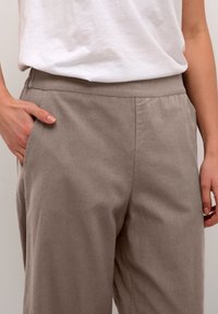 Pantalons en lin gris avec une coupe décontractée, dotés de poches latérales et d'une texture lisse. La taille est élastiquée pour plus de confort.