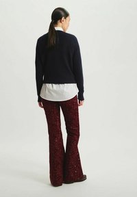 Un pull en maille bleu marine sur une chemise blanche, accompagné de pantalons évasés recouverts de sequins rouges. La tenue se distingue par sa texture et sa coupe ample.