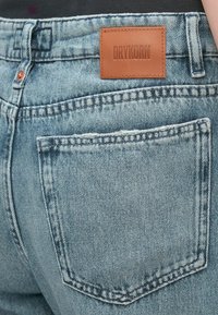 Světle modré džínové kalhoty s třepícími se okraji, koženou zadní nášivkou označenou "DRYKORN", kontrastním šitím a jednou zadní kapsou.