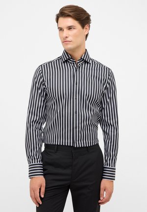 Schwarz-weißer gestreifter Button-Up-Hemd mit Kragen, langen Ärmeln und kontrastierenden gestreiften Manschetten, getragen mit schwarzen Hosen.