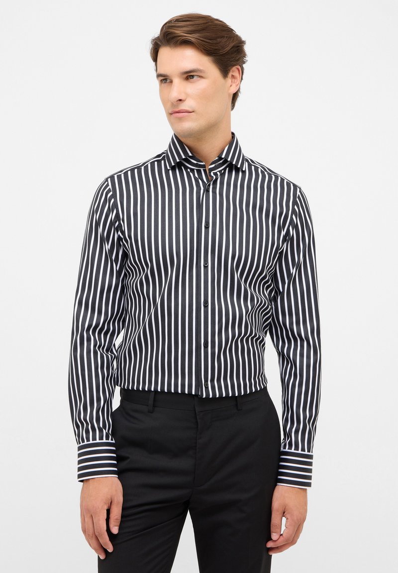 Zwart-wit gestreepte button-up shirt met een kraag, lange mouwen en contrasterende gestreepte manchetten, gedragen met zwarte broeken.