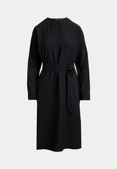 Mustapaitainen pitkähihaiseksi mekko, jossa on korkea kaulus, vyötäröllä vyö ja suora siluetti. Valmistettu sileästä kankaasta, takana on nappikiinnitys.