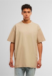 Beige bomull T-skjorte med avslappet passform, rund hals og kortermede ermer. Enkelt design uten synlige mønstre eller detaljer.