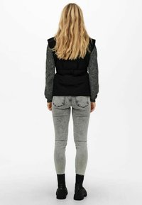 Černá vycpaná vesta s přezkou, šedé texturované rukávy, šedé úzké džíny a černé kotníkové boty. Hladká látka a ležérní design.