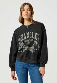 Czarny sweter z grafiką przedstawiającą tygrysa, szachownicowe flagi i napis "WRANGLER MOTORCYCLE CLUB". Dół oraz mankiety zakończone ściągaczem.