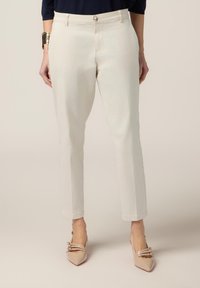 Pantalons sur mesure beige clair avec une texture lisse, dotés d'une fermeture à bouton et d'une coupe ajustée. Associés à des ballerines beiges à bouts pointus.