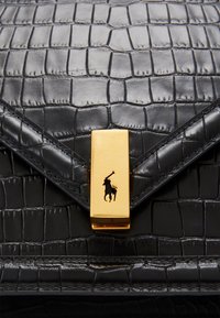 Czarna torba ze skóry wytłaczanej w wzór krokodylej skóry, z złotym zapięciem magnetycznym z czarnym logo konia. Gładka faktura z geometrycznymi detalami.
