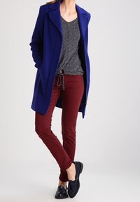 Námořnický vlněný kabát, top s puntíky, vínové kalhoty a černé boty. Kabát má límeček a přiléhavý střih; kalhoty jsou slim-fit.