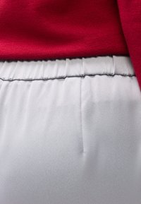 Κοντινό πλάνο κόκκινου πλεχτού πουλόβερ που είναι μπαλωμένο μέσα σε παντελόνι με ανοιχτό γκρι ελαστική μέση και υφή από λείο ύφασμα.