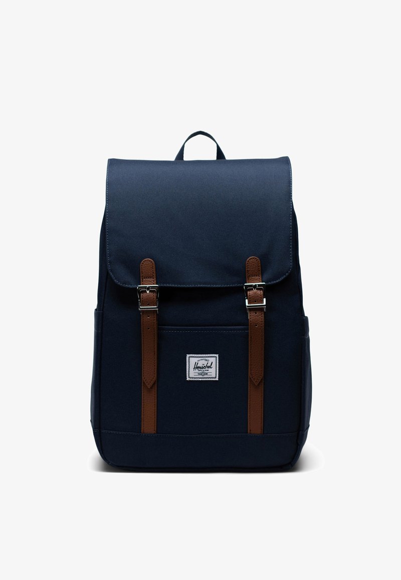 Marine canvas rugzak met bruine leren banden en metalen gespen, ontwerp met bovenklep, voorvak en een klein merkembleem.