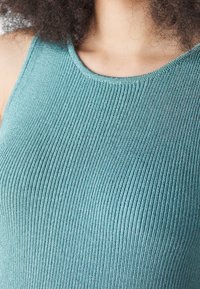 Canotta a coste in tessuto teal, con scollatura arrotondata e un design aderente che mette in risalto texture e dettagli del materiale.