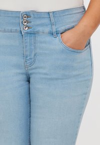 Light blue denim jeans with a high waist, featuring three metal buttons, a front pocket, and smooth texture.