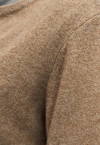 Κοντινή λήψη καφέ υφασμάτινου πλεκτού με υφή, που δείχνει λεπτομερείς ραφές και μαλακή, χνουδωτή επιφάνεια.