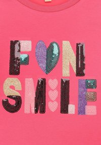 Rosa Hemd mit einem glitzernden "FUN SMILE"-Text, erweitert um ein lila Herz und verschiedene Formen in metallischen und glitzernden Ausführungen. Weicher Stoff.
