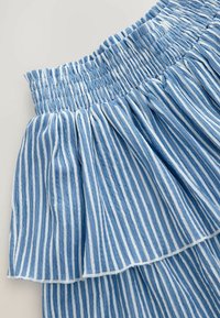 Jupe rayée bleue et blanche avec une taille smockée et un design en couches de volants. Le tissu semble léger et texturé.