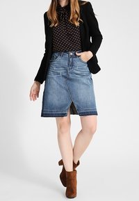 Denimhame, jossa on etuavoin, haalistunut sininen väri ja risatetut reunat. Yhdistetty mustan puseron kanssa, jossa on pilkkuja, ja ruskeiden nilkkureiden kanssa.