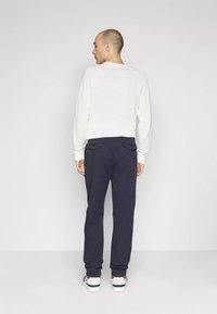 Felpa bianca a trama con maniche raglan, abbinata a pantaloni blu navy con tasche laterali e sneakers bianche con dettagli.