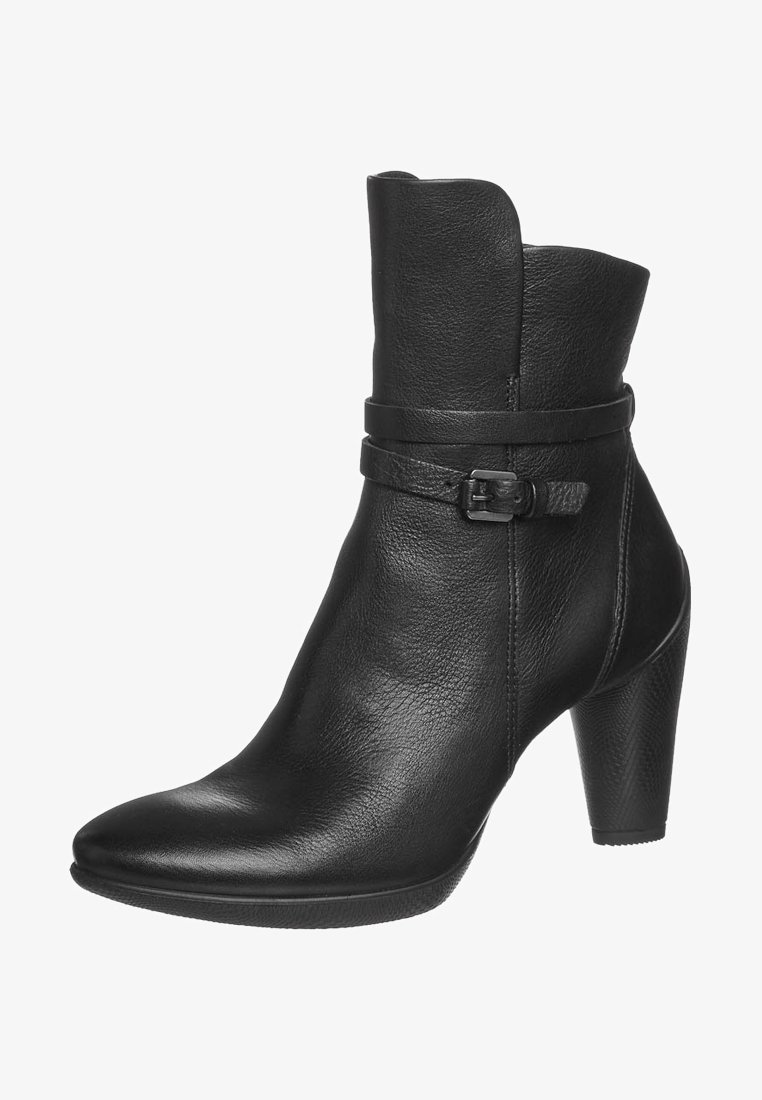 Bottine en cuir noir avec bout pointu, talon bloc de hauteur moyenne, et sangle décorative avec boucle autour de la cheville.
