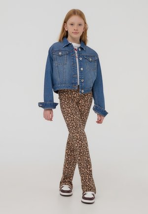 Giacca di denim con due tasche sul petto, di colore azzurro chiaro; abbinata a pantaloni svasati con stampa leopardata e sneaker marroni e bianche.