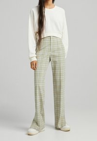 Biały krótki sweatshirt zestawiony z jasnoszarymi spodniami w kratę o wysokim stanie. Spodnie mają ciemne linie w kratę i rozszerzający się krój.