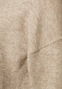 Beige neulottu kangas, jossa on sileä rakenne ja hienovarainen kuvio. Materiaali näyttää pehmeältä ja kevyeltä, mikä tekee siitä ihanteellisen kerroksittain käytettäväksi.