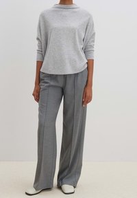 Svetle šedý oversize svetr s vysokým výstřihem, doplněný o šedé kalhoty s širokými nohavicemi a krémové boty.