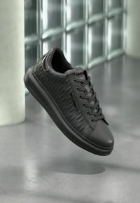 Černé tenisky s texturovaným vzorem houndstooth, hladkým koženým svrškem, kulatou špičkou a tkaničkami. Lehké podešev pro pohodlí a styl.