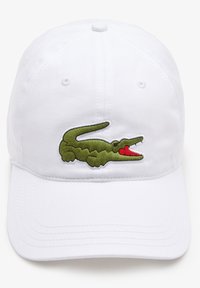 Biała czapka bejsbolowa z zielonym haftowanym logo krokodyla z przodu. Materiał zdaje się być bawełniany o gładkiej fakturze.