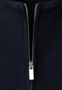 Nærbillede af delvist åben sølvmetal lynlås på mørkeblå tekstureret stof.