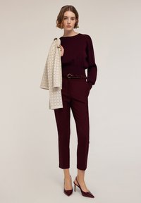 Pulover tricotat bordeaux și pantaloni, acompaniați de o jachetă crem cu buline negre. Pantofii cu toc înalt bordeaux completează ținuta.