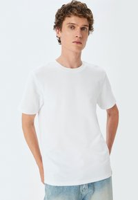 Hvid T-shirt med korte ærmer, rund hals, struktureret stof, løs pasform, parret med lyseblå denimshorts. Simpelt, ensfarvet design uden mønstre.